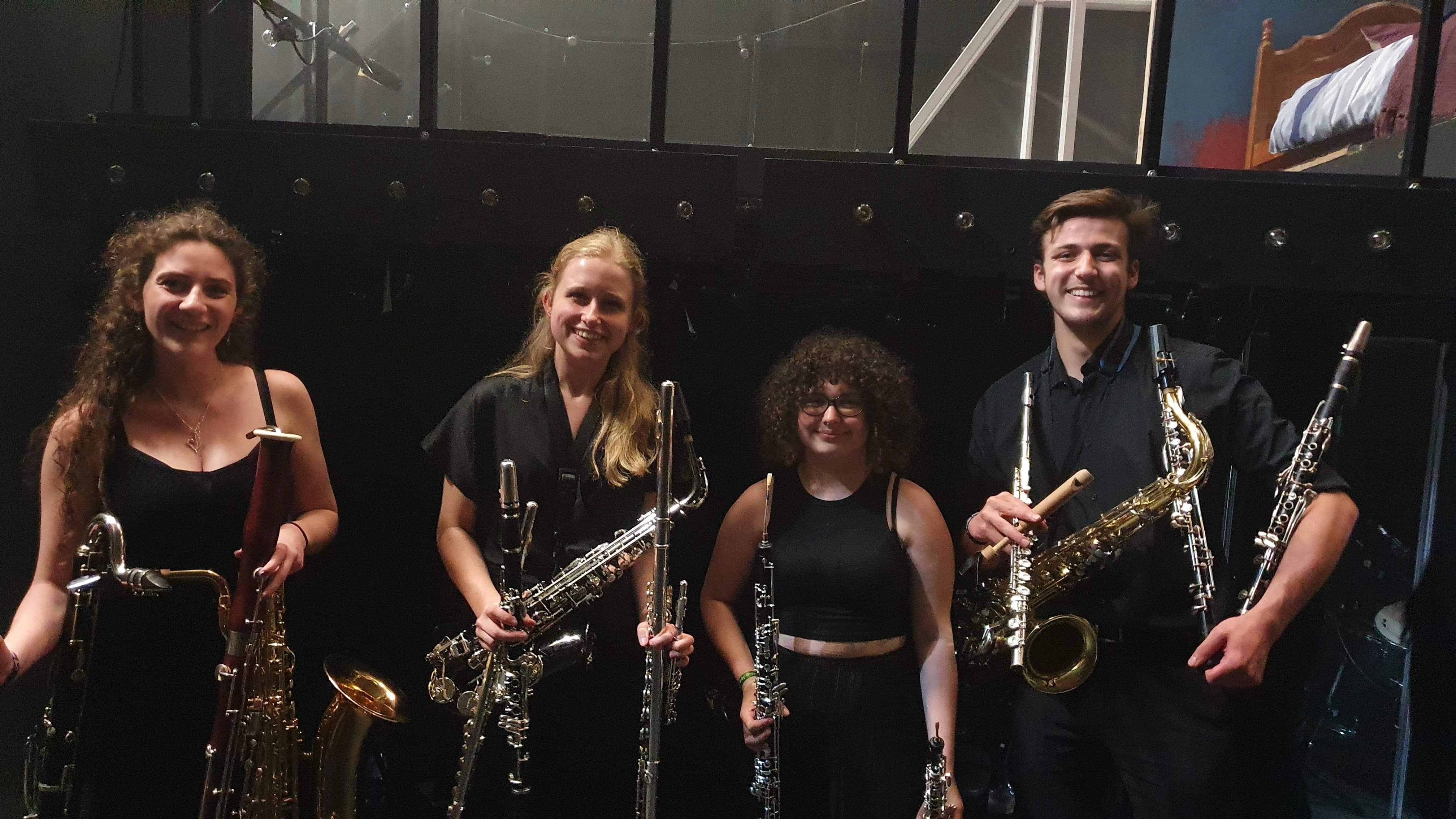Jonathan Parapadakis holding flute, clarinet, oboe, tenor saxophone and slide whistle for musical theatre show Company. Also pictured are Georgia Rawlins (flute, piccolo, alto flute, clarinet, alto saxophone) and Kirsty Ryall (bassoon, bass clarinet, baritone saxophone).